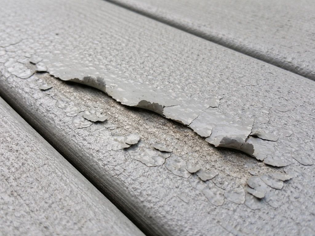 Close-up of an acrylic-coated deck surface with early peeling and flaking near glossy edges